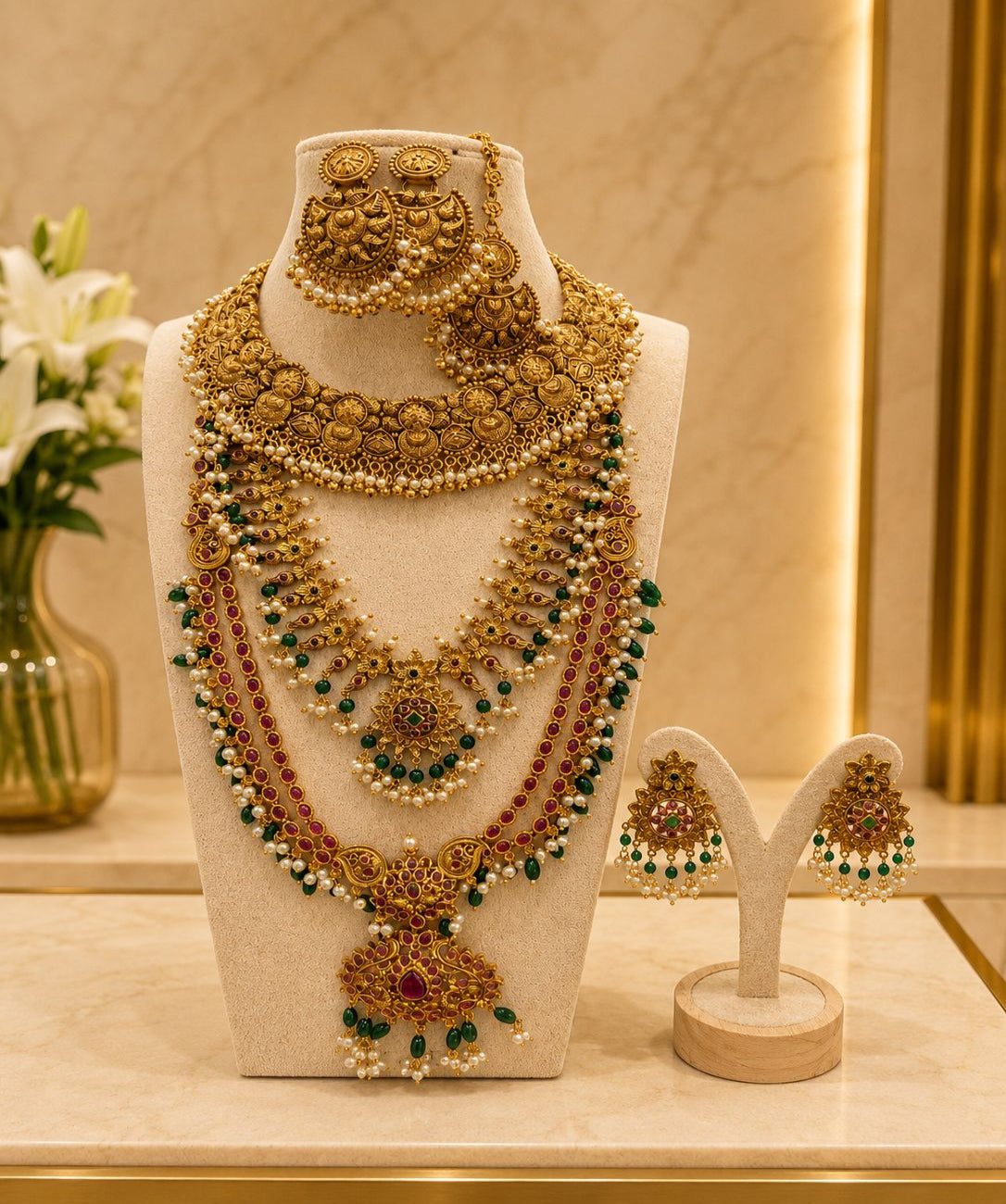 Temple bridal jewellery set with antique gold finish, Lakshmi motifs, ruby and green stones, pearl detailing, matching earrings, and maang tikka.